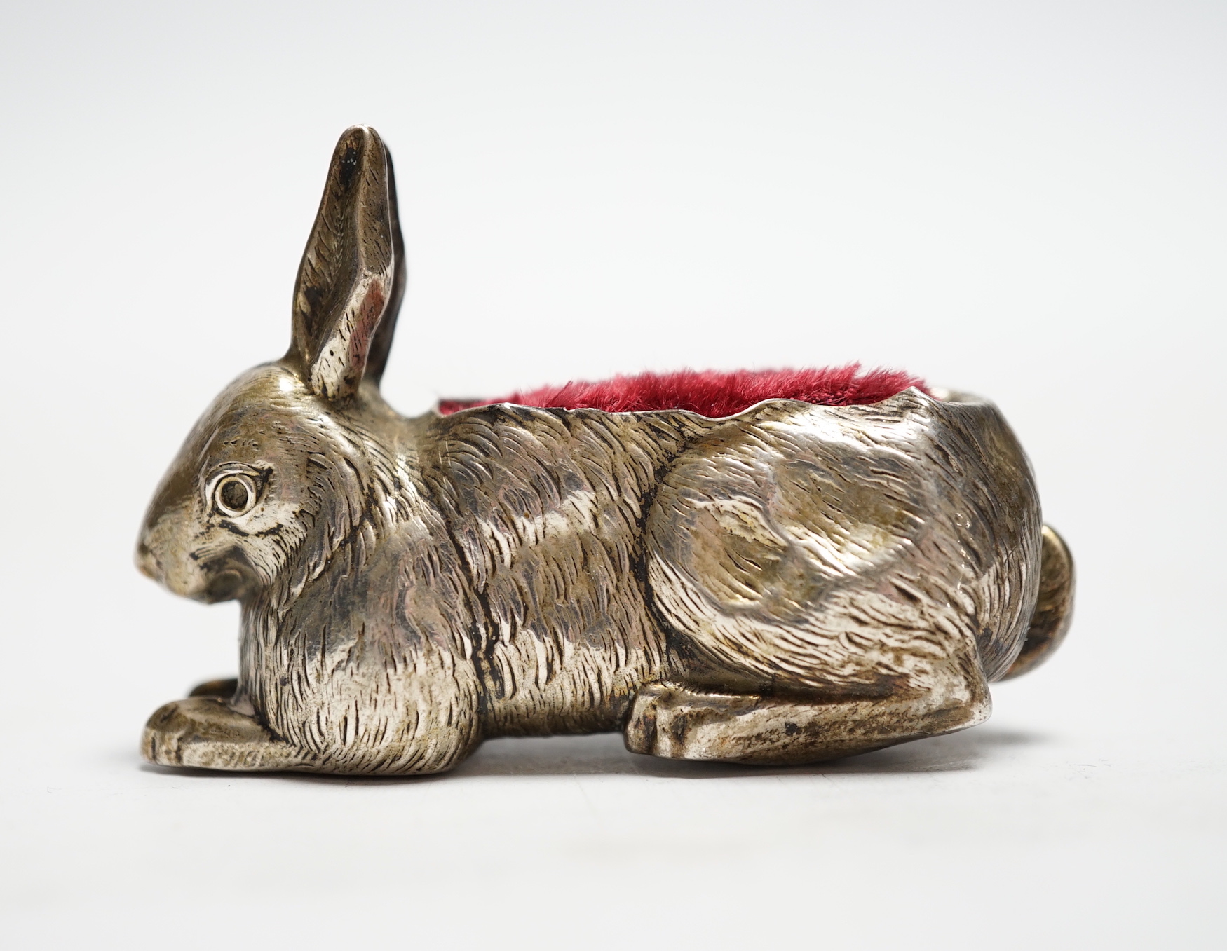 An Edwardian novelty silver mounted pin cushion, modelled as a recumbent rabbit, Henry Matthews, Birmingham, 1907, 64mm.